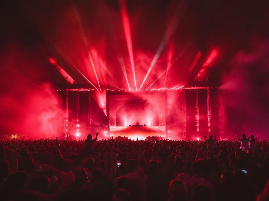 Festival crowd under red stage beams and fog